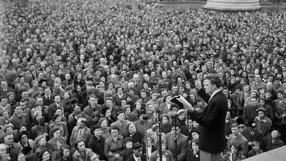 Evangelist Billy Graham, on stage, addresses a crowd.