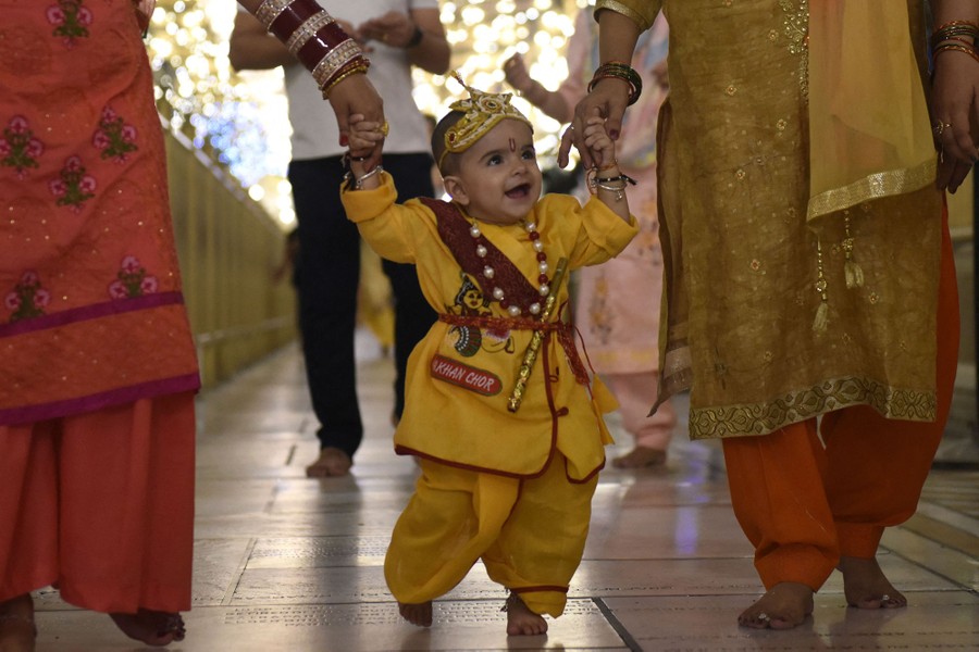 Parents hold the hands of a young child dressed in a colorful costume.