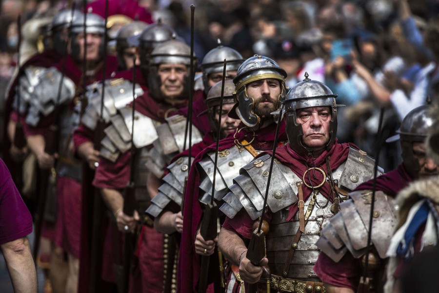 More than a dozen men dressed as ancient Roman soldiers march in a line.