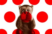 A statuette of a monkey covering its mouth, overlaid with red polka dots