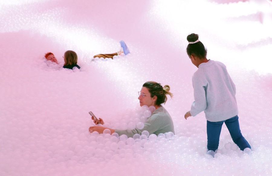 Several people play in a huge ball pit, surrounded by thousands of baseball-size, clear plastic balls.