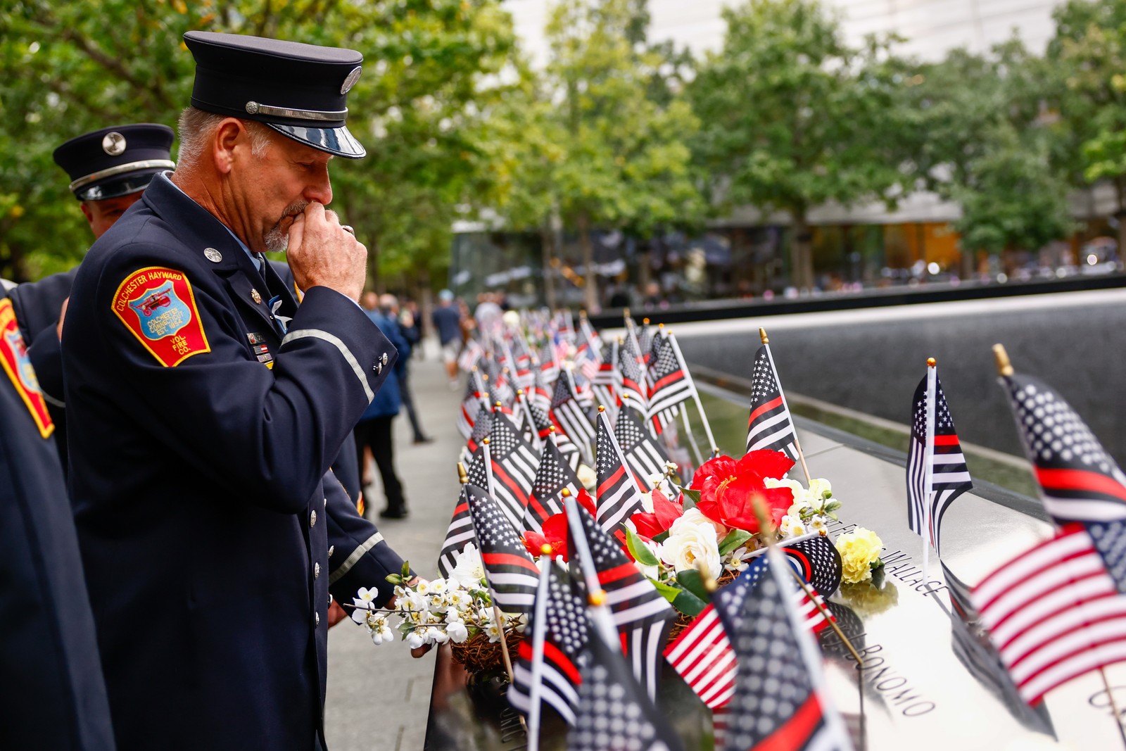 Firefighters pay their respects at the reflecting pools in New York City, standing near dozens of small American flags placed nearby.