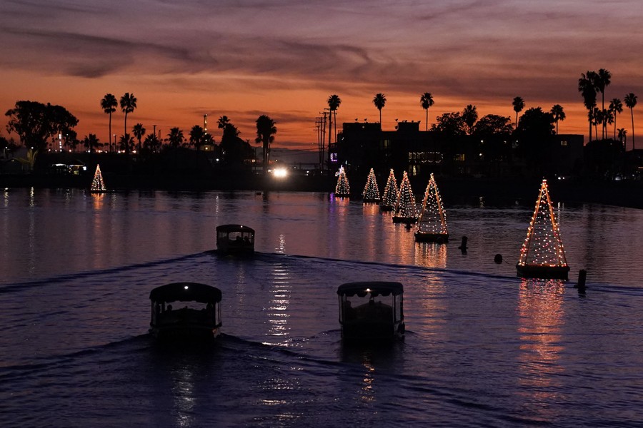 Boats make their way past floating Christmas tree lights at sunset.