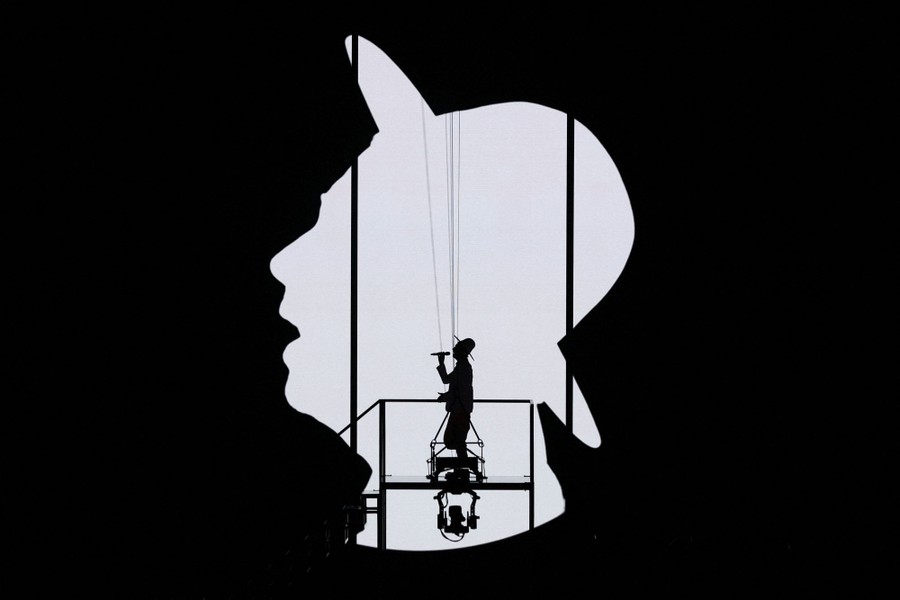 A singer performs in front of a large screen projection of the outline of their head and hat.