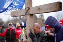 Supporters of President Donald Trump pray outside the U.S. Capitol on January 6, leaning on a large wooden cross.