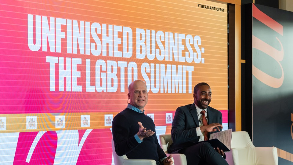 Two men at The Atlantic Festival in front of a sign that reads "Unfinished Business: The LGBTQ Summit."