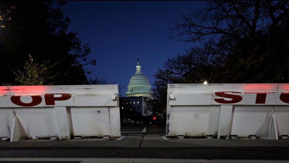 At night, the U.S. Capitol is visible in the background, with large white barricades with the word "Stop" in the foreground.