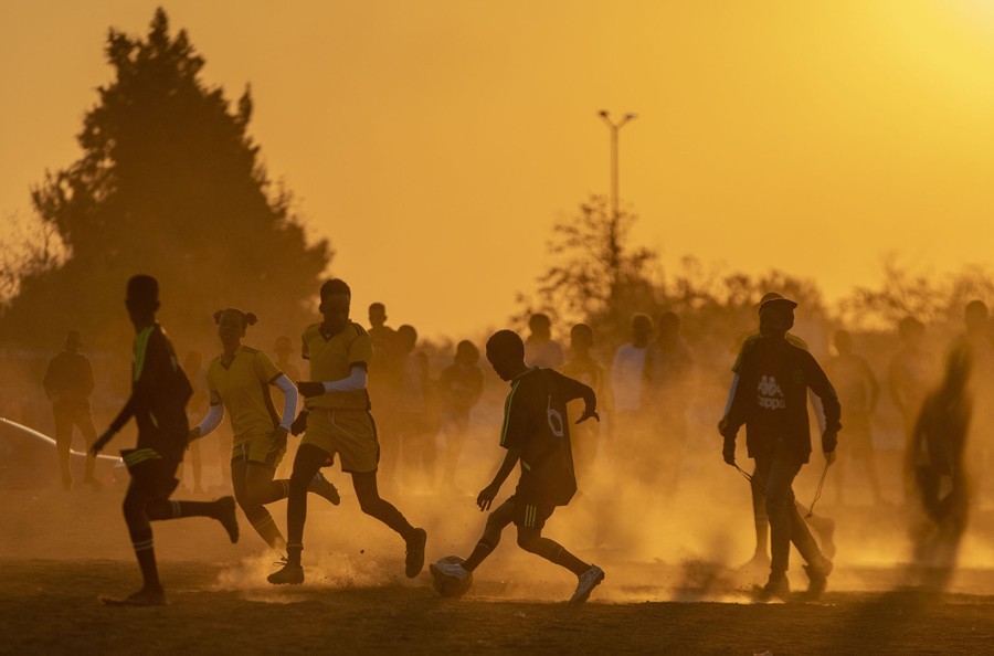 Soccer players play a match on a dusty soccer field.