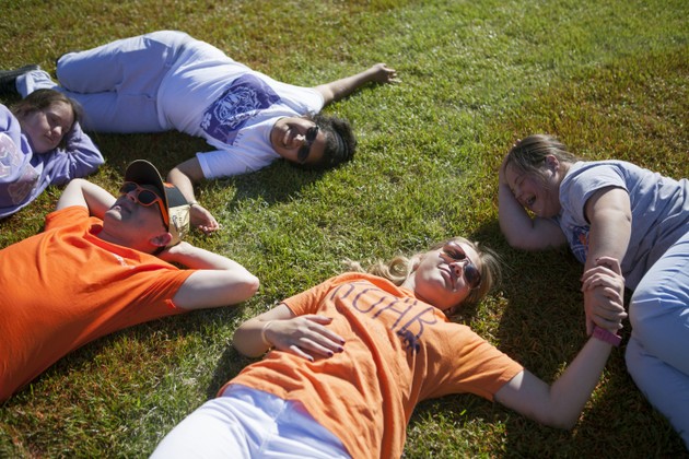 Five students smile and lay down in the grass
