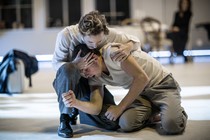 Two men in white clothes embrace on a stage.
