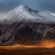 A distant view of a mountain with a dusting of early-season snow across the top, and a bright patch of sunlight on the valley floor below