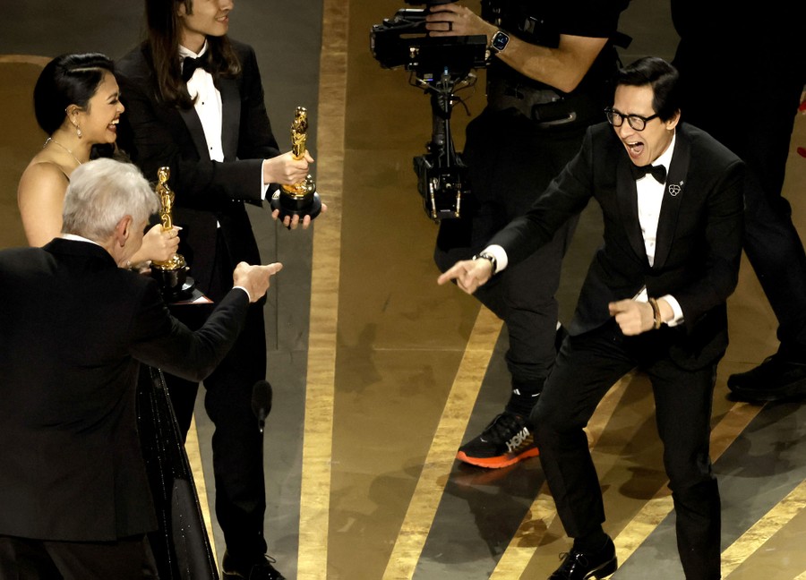 Actors Harrison Ford and Ke Huy Quan smile and point at each other onstage as Oscar statuettes are presented.
