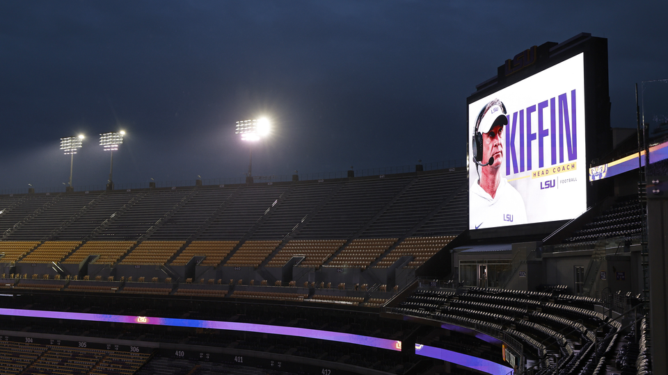 Photograph of an empty stadium at night with a giant screen showing Lane Kiffin's name and photo as head coach of Louisiana State University