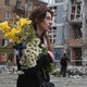 A woman holding flowers walks by the rubble of a bombed out apartment building