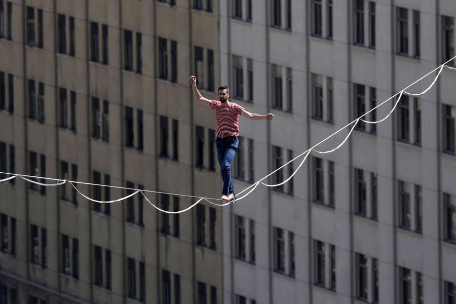 A tightrope walker, mid-walk, among tall buildings