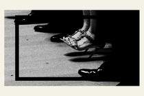 A photo showing men's shoes with one woman wearing heels sitting between them