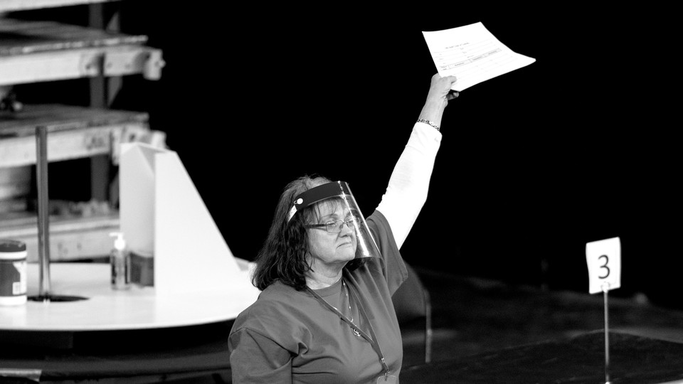 A woman wearing a clear face shield holds up a piece of paper. She is a contractor working to count ballots during the Arizona election recount.