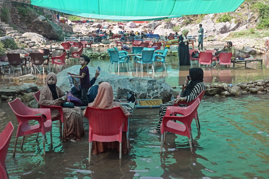 Several people sit in chairs underneath a tarp in shallow pools of water.