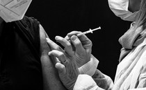 a vaccine being injected into an arm. both people in the photo are wearing masks. the tops of their faces are not visible.