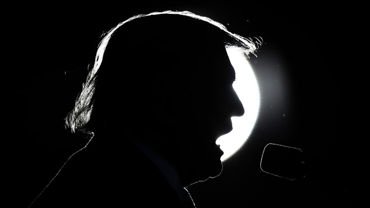 Donald Trump's head silhouetted against a spotlight as he speaks into a microphone