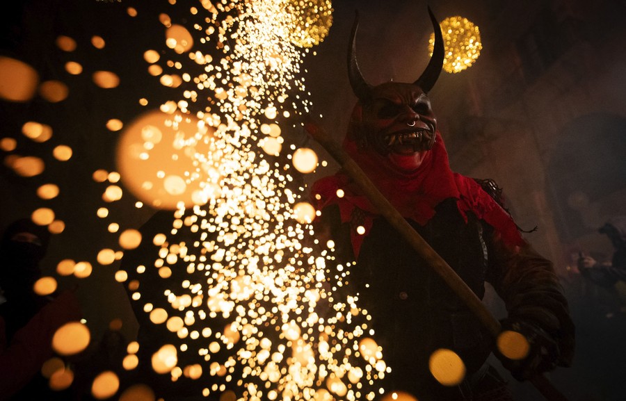 A person dressed as a demon carries a sparking firework on a stick.