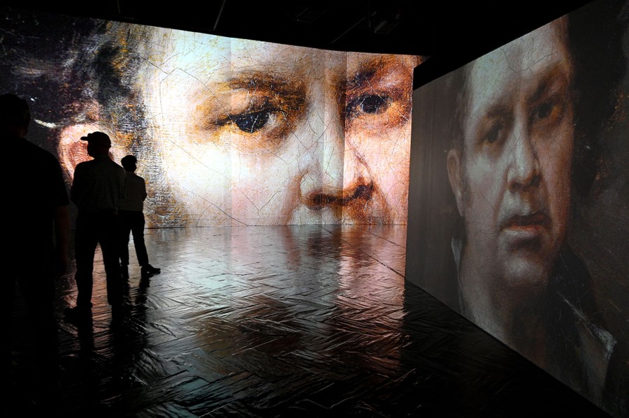 People stand in a room looking at large projections of paintings.