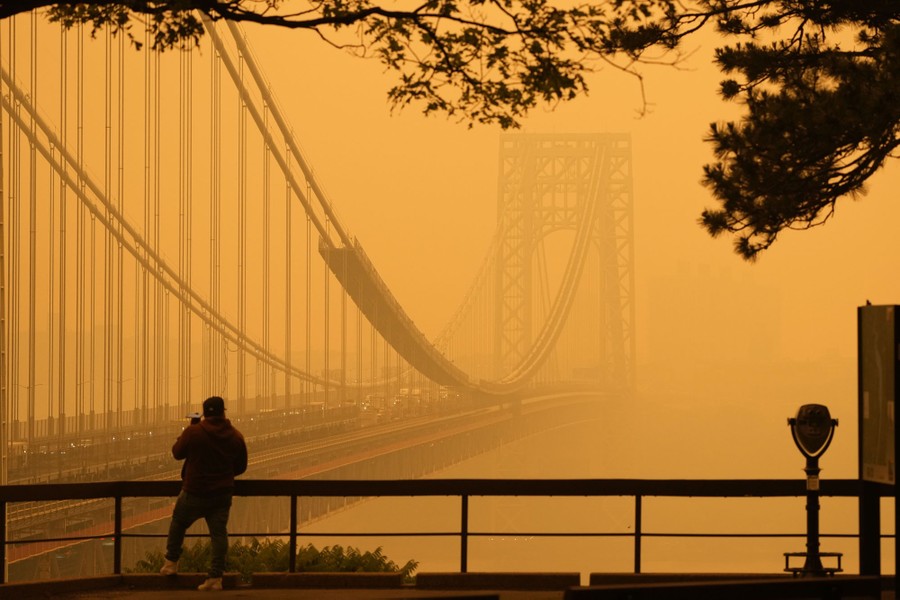 A person stands near a huge suspension bridge that vanishes into an orangish haze.