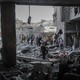 A rubble-filled area of Gaza is seen from inside a bombed building, with people walking around inspecting the rubble.