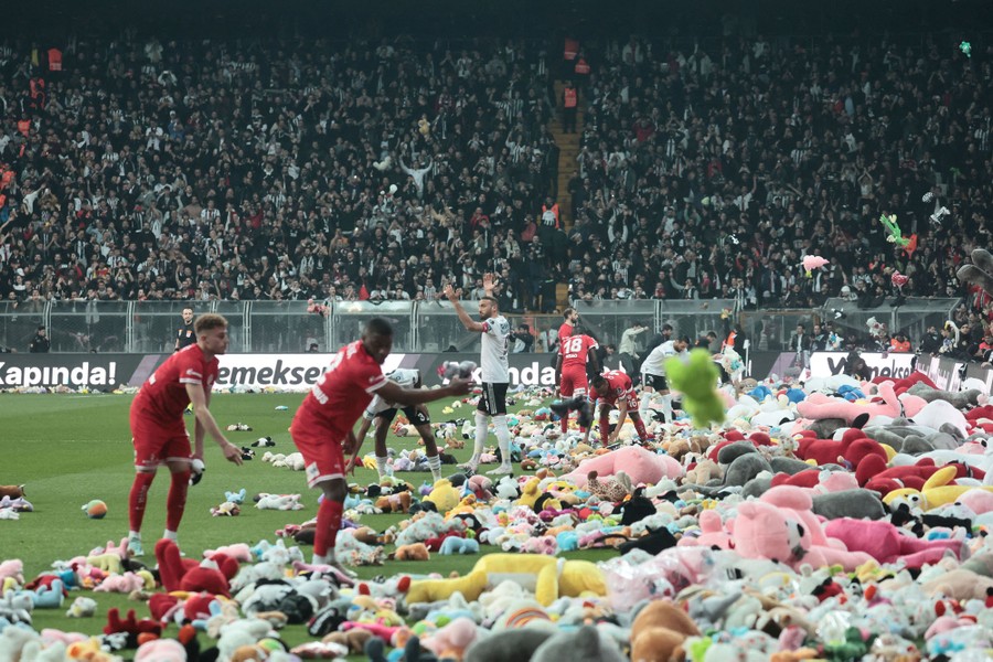 A soccer field in a stadium is partially buried under piles of stuffed animals and toys thrown by fans.