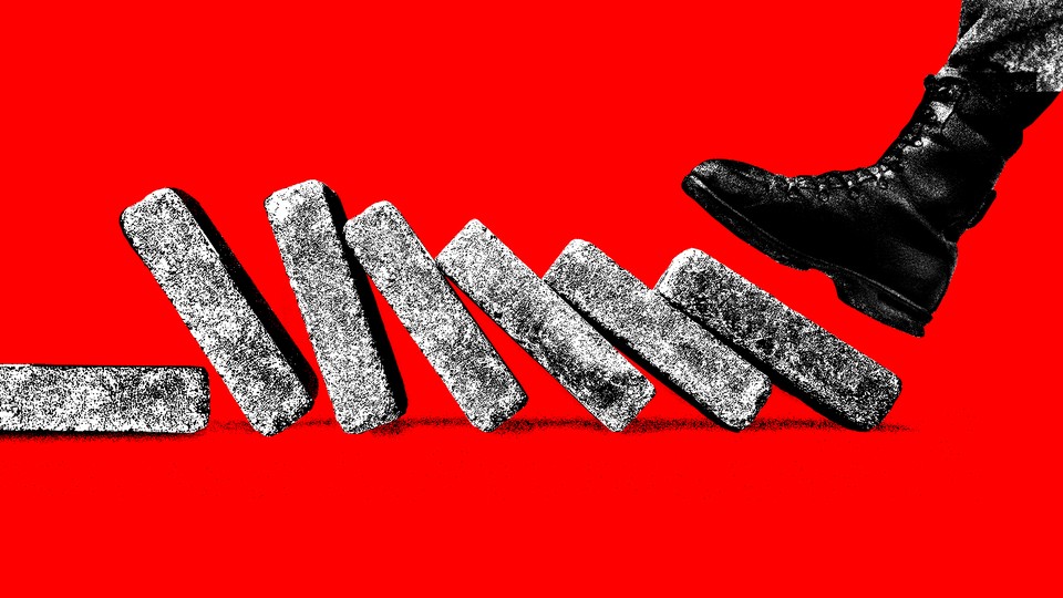 A foot in a military boot comes down on the first of a line of bricks set up like dominoes to topple