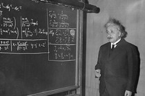 A black and white photograph of Albert Einstein in front of a blackboard