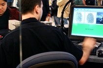 A U.S. Customs and Border Protection agent checks an overseas visitor's fingerprints and image in a database.