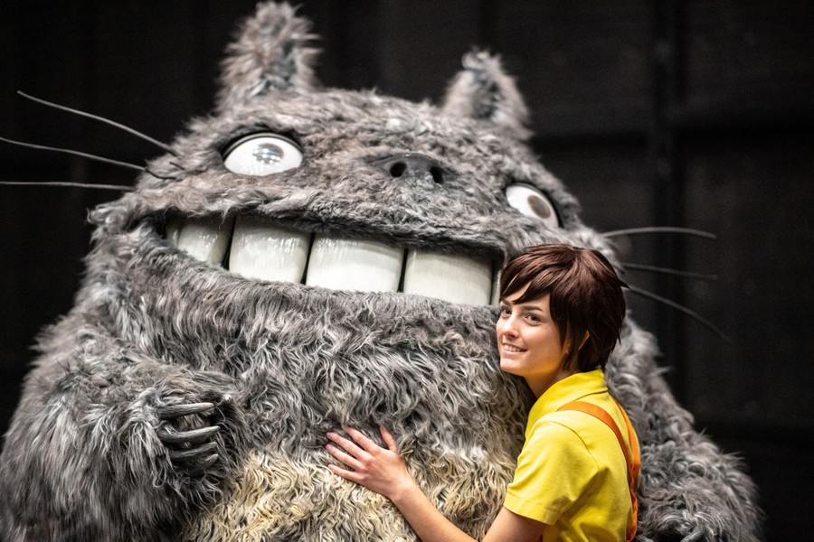 A person in costume poses beside someone in a much larger full-body costume depicting the character Totoro, from the movie "My Neighbor Totoro."