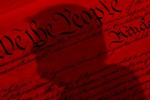 A red-tinted United States constitution with the shadow of Donald Trump's bust over it