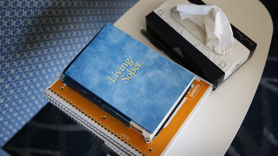 A book titled "Living Sober," spiral notebooks, and a tissue box on a table