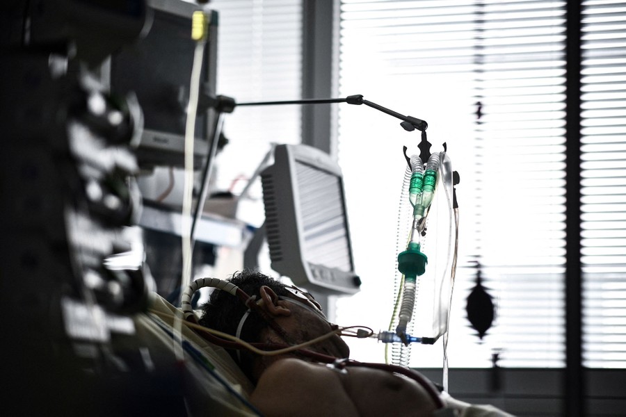 A person lies in a hospital bed, surrounded by medical equipment.