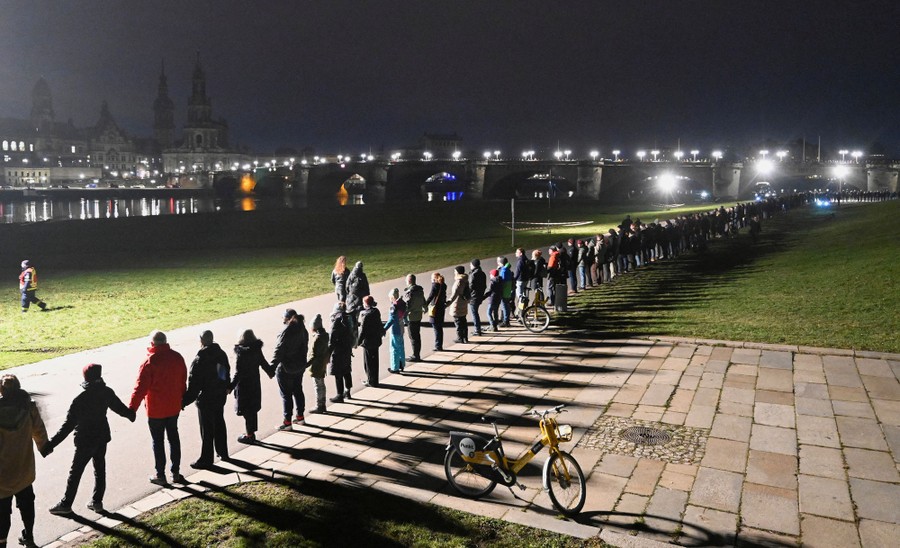 People form a human chain during a memorial event along a riverbank.