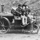 Three people riding in an 1860s Rickets steam carriage.