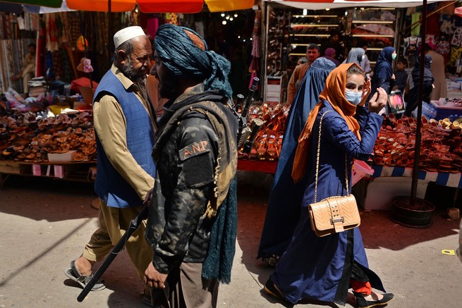 A Taliban fighter carrying a gun passes female shoppers at a market in Kabul.