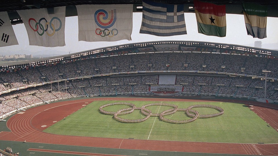 Flags frame the Olympic Stadium as participants form the Olympic rings on the field.