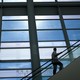 A man on an escalator looks at an enormous set of windows.