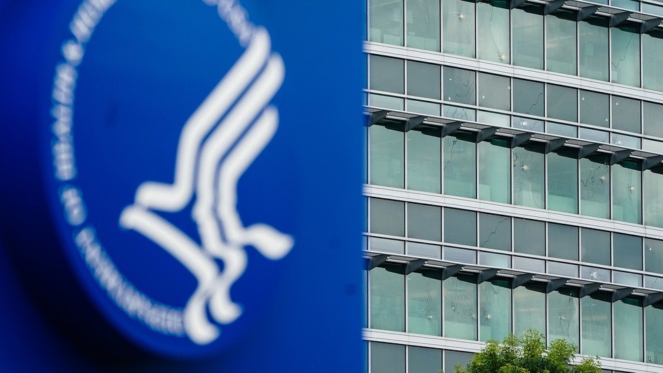 Photograph of a blurry sign with the CDC's logo in front of the bullet-hole-riddled windows of a CDC building