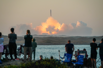 Spectators watch as SpaceX's Starship lifts off in a cloud of fire and smoke from the Gulf Coast