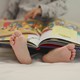 A small child reading a picture book on a bed