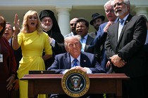 Trump sits at a desk surrounded by faith leaders