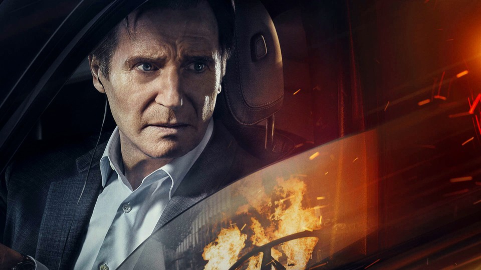 Liam Neeson in a car, looking at a fire outside