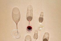Photograph of eight partially full wine glasses casting shadows on a beige background
