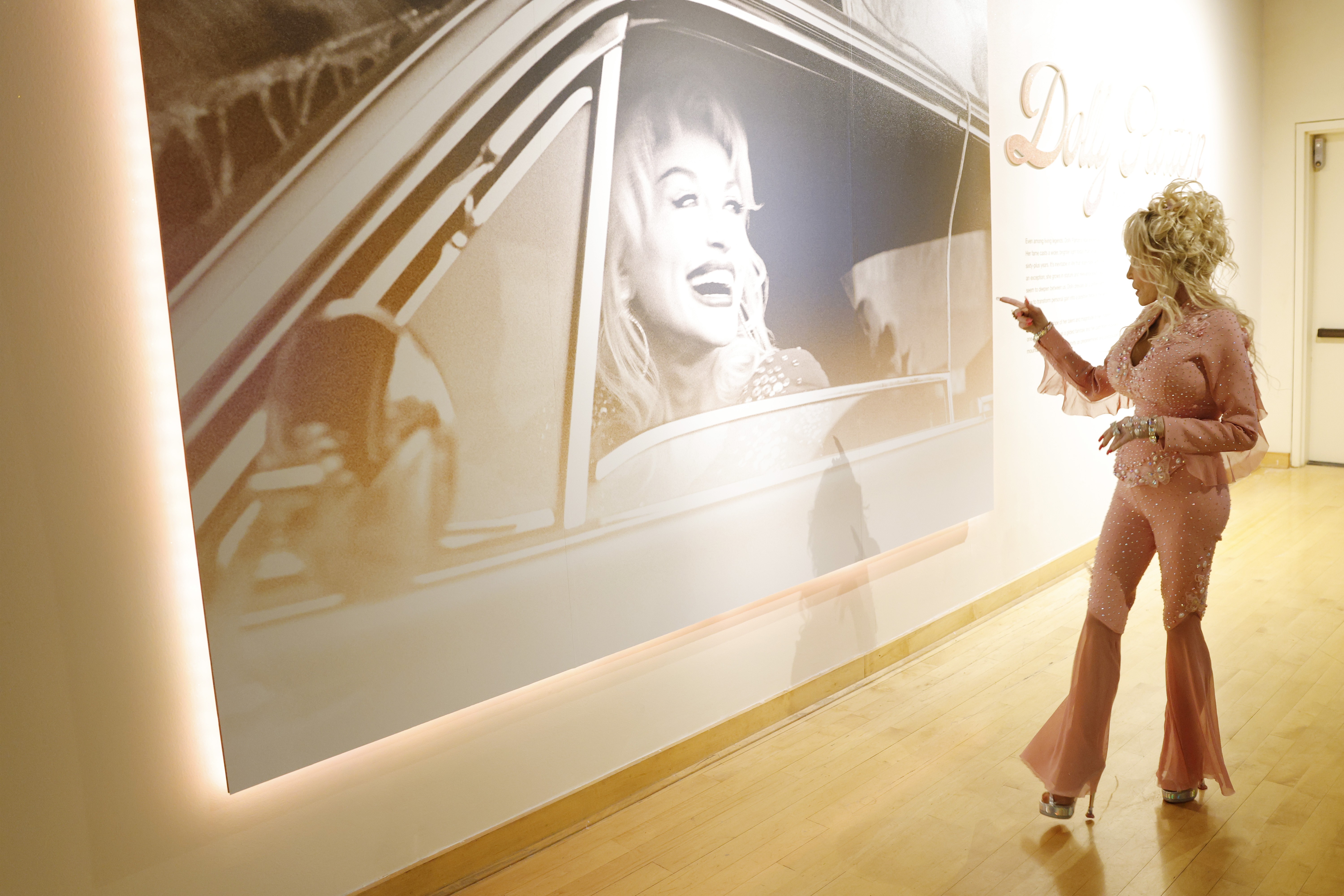Dolly Parton points at a large photo of herself at the opening of an exhibit.