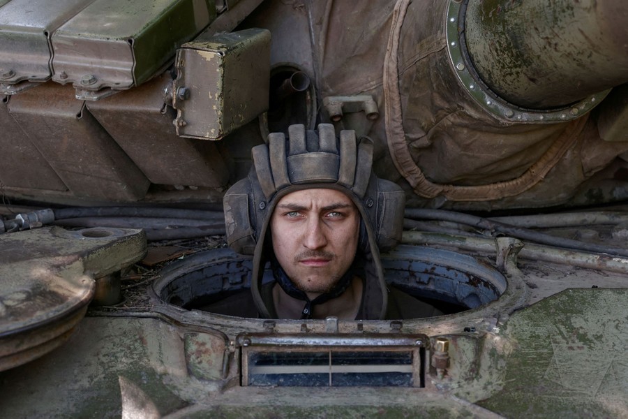 A soldier pokes his head out of an opening in the tank he is seated in.