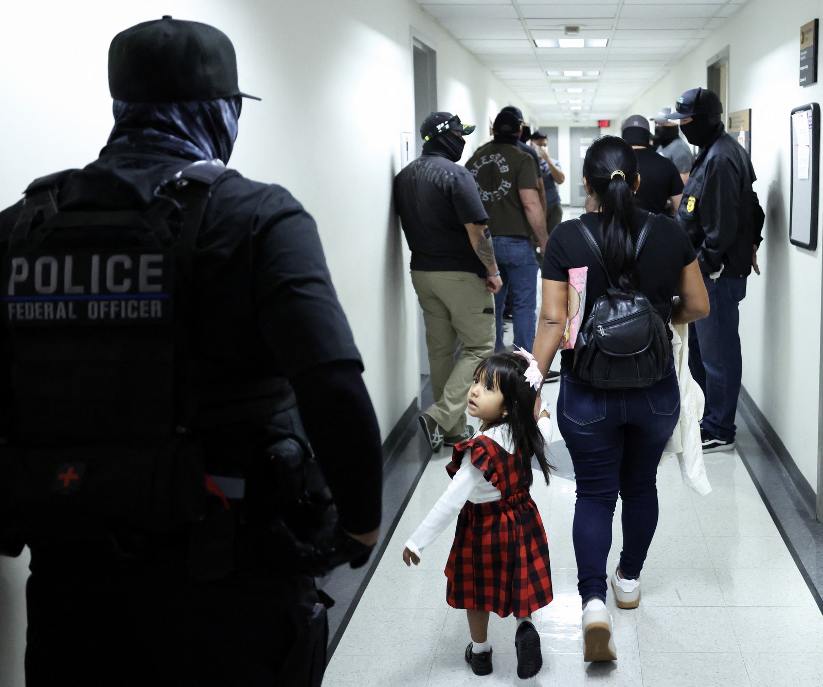 A woman and her child walk through a hallway outside of a courtroom, as federal agents patrol the hallways.
